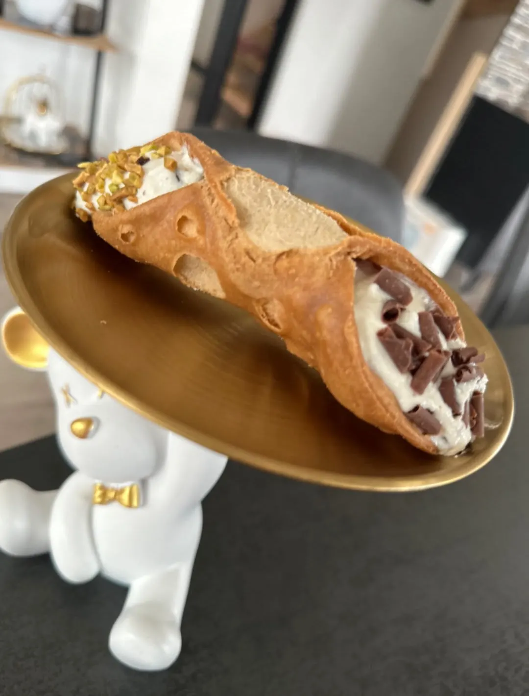 Un cannoli fourré à la crème et aux pépites de chocolat, sur un plateau doré