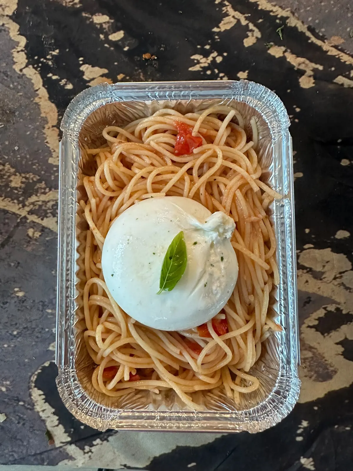 Des spaghetti à la tomate surmontés d'une burrata et d'une feuille de basilic