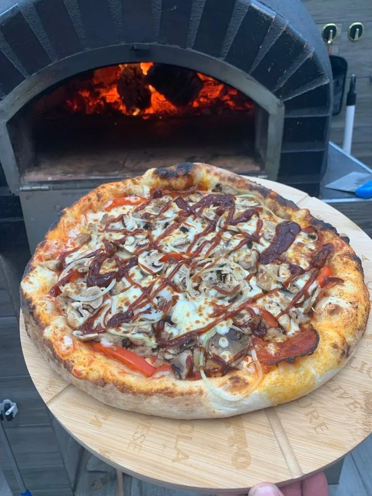 Une pizza aux champignons et à la sauce barbecue, présentée devant la bouche du four