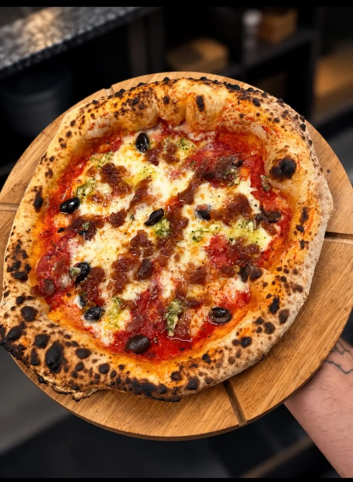 Une pizza tomate-mozzarella aux olives noires et à l'ail persillé, au bord bien cuit, sur une planche en bois