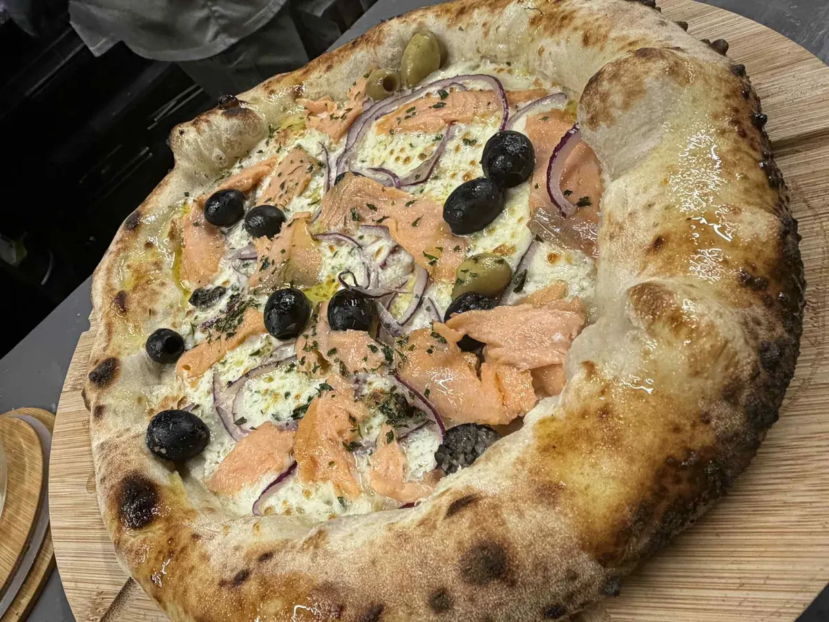 Une pizza au saumon, aux olives noires et aux oignons rouges
