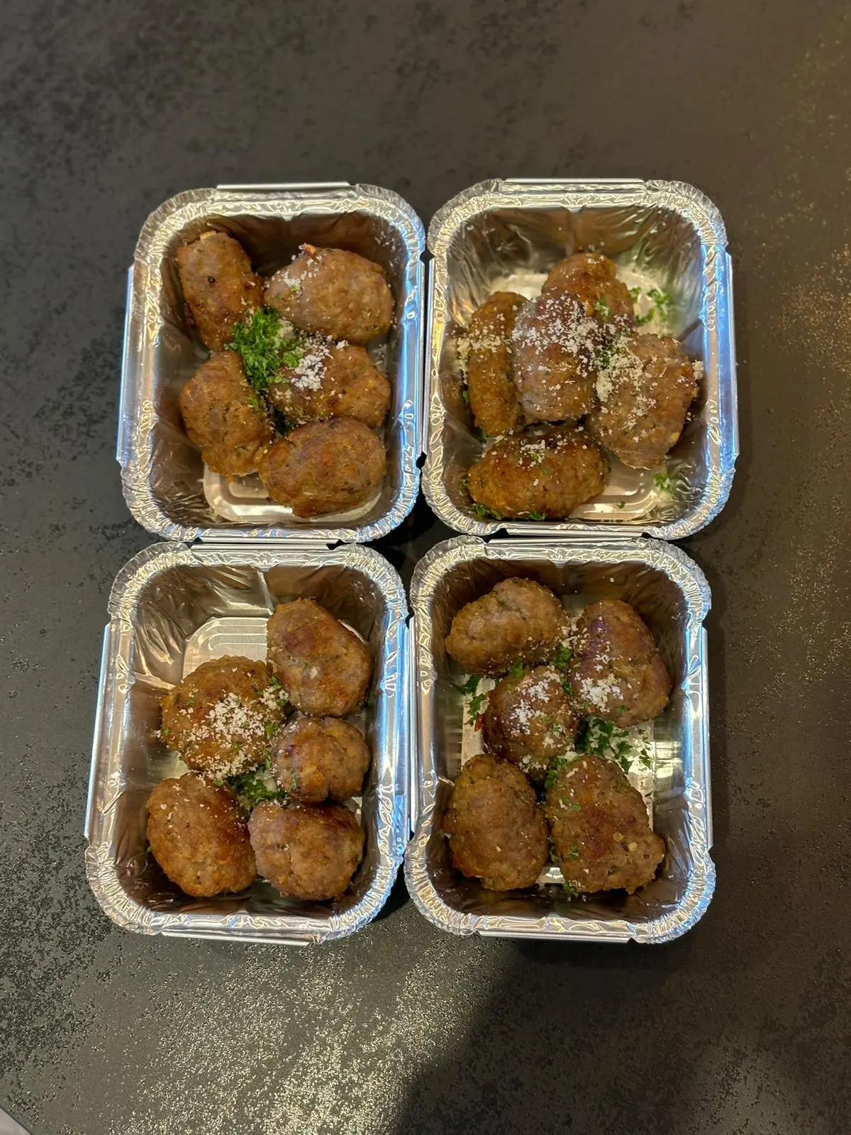 Quatre barquettes de boulettes de viande en sauce, parsemées de parmesan