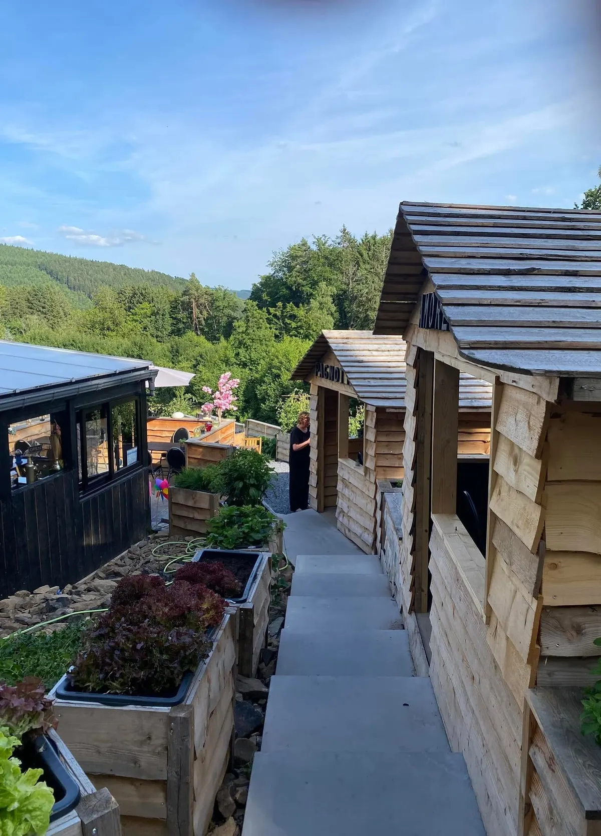 Les petites cabanes en bois de la terrasse, au bord d'une allée de pierre, avec les collines boisées de la vallée en arrière-plan