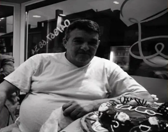 Vito, en noir et blanc, assis à une table de restaurant devant un gâteau